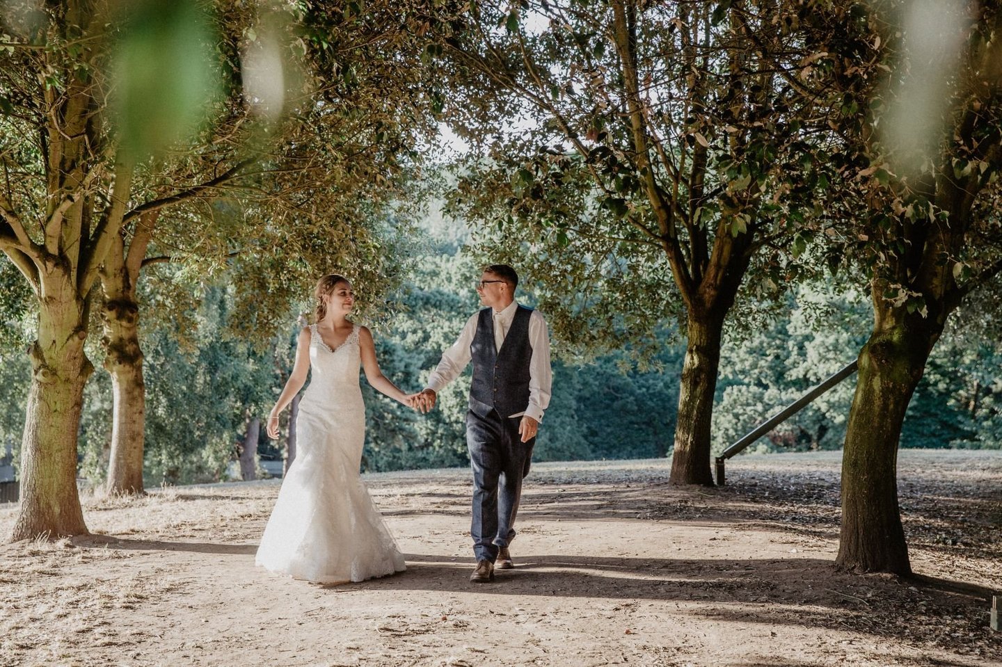 Bride and groom walk through forest holding hands 