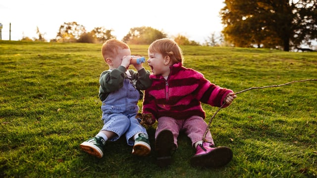 Image of iris & axel kids facing eath other sat on grass web 1920x1080