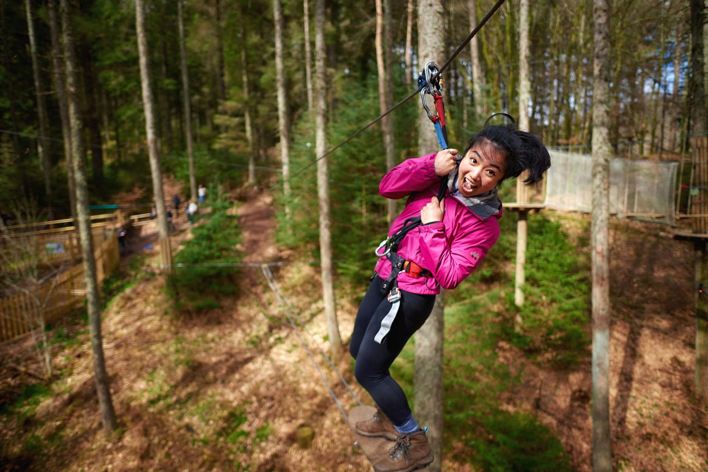 Young woman ziplines across forest screaming happily