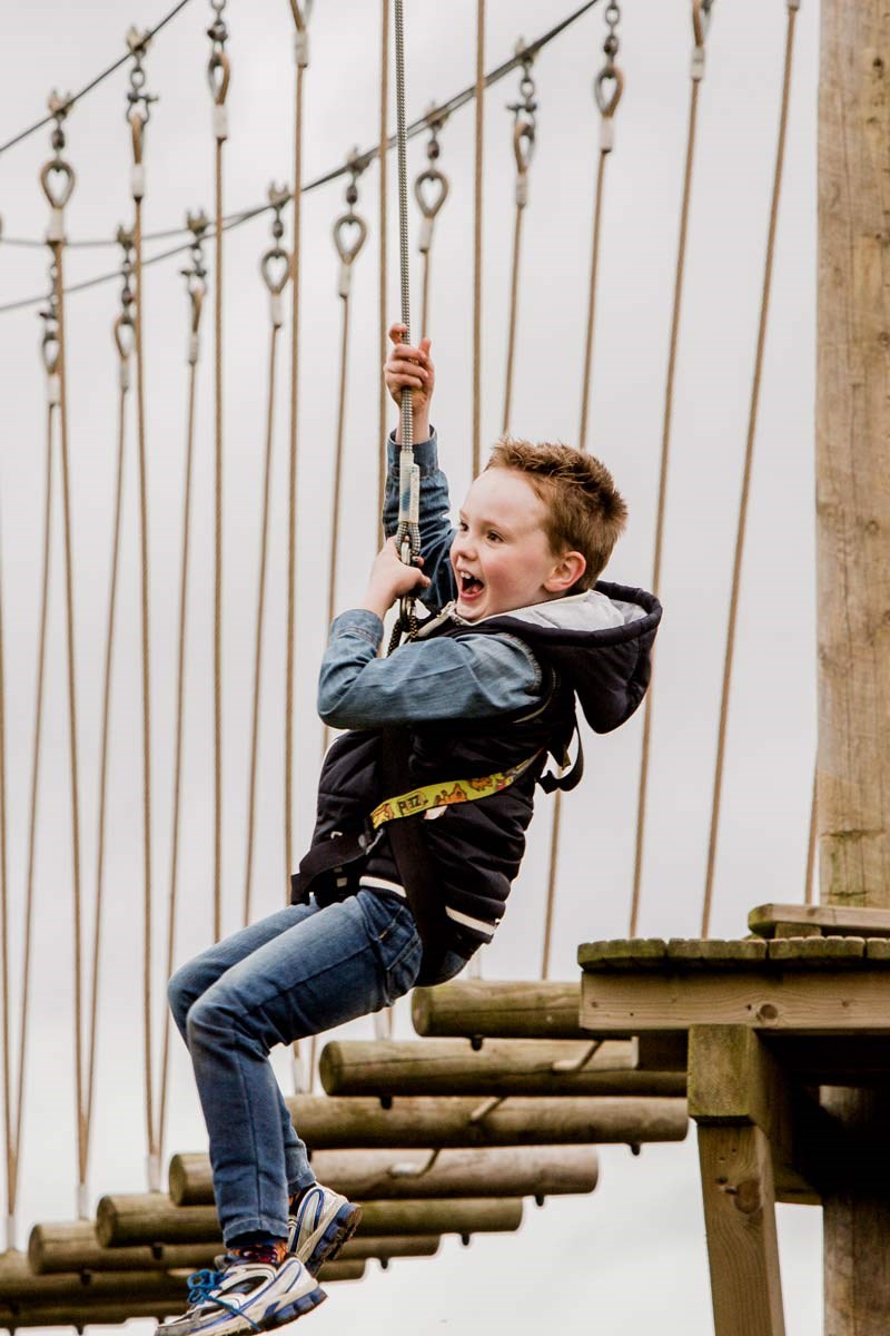 Child screams happily while ziplining on high ropes course 